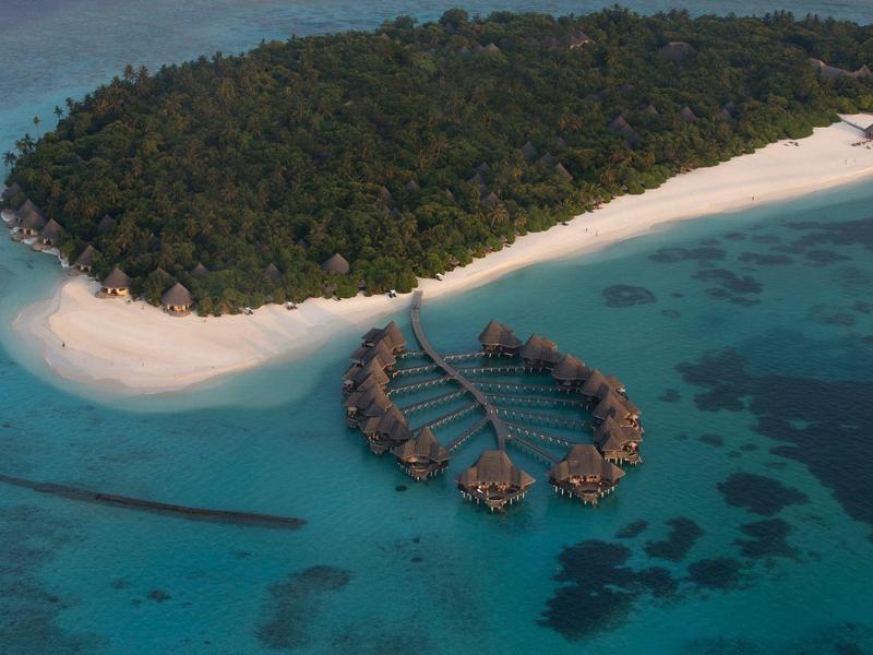 Insel mit üppiger Vegetation und Bungalows auf Stelzen im türkisfarbenen Wasser.