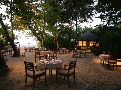 Cena romántica al aire libre en la playa con mesas iluminadas y árboles