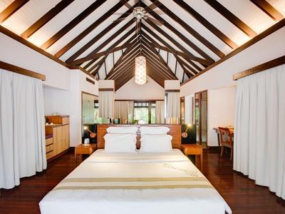 Helles Schlafzimmer mit hohem Holzbalkendach, großem Bett und weißen Vorhängen an den Seiten.