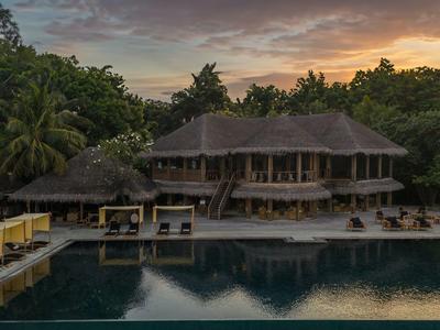 Luxuriöses Hotel mit Pool, umgeben von Palmen und üppiger Vegetation bei Sonnenuntergang.