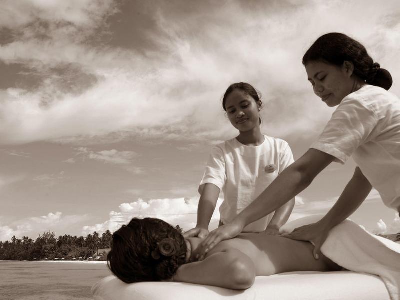 Türkisblaues Wasser, weißer Sandstrand und Stege zu Bungalows über dem Meer bei klarem Himmel.