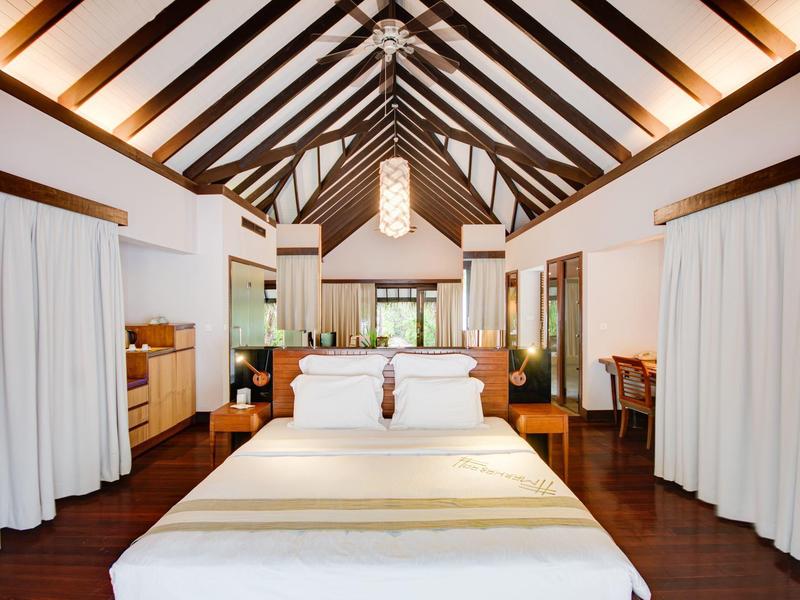 Helles Schlafzimmer mit hohem Holzbalkendach, großem Bett und weißen Vorhängen an den Seiten.