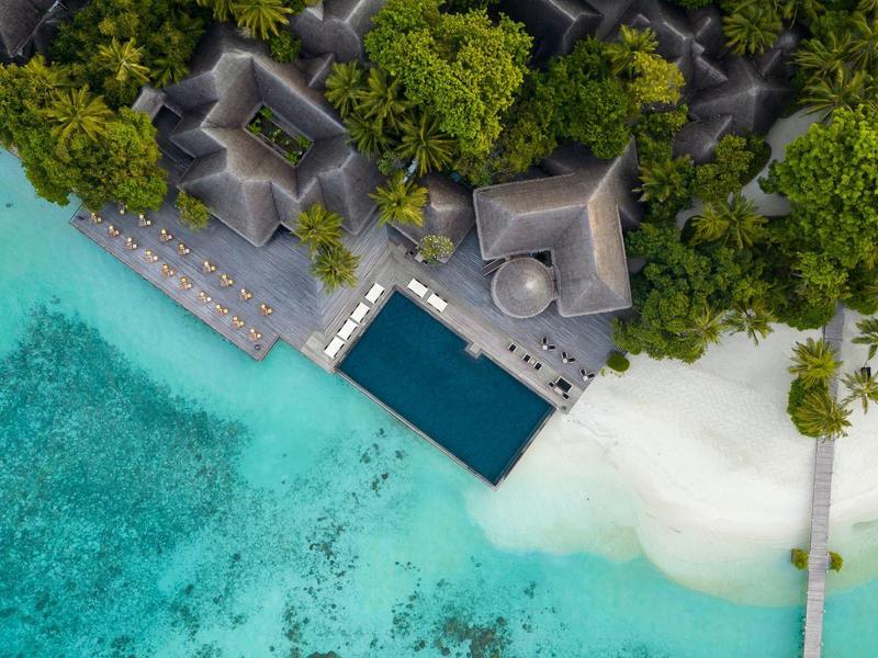 Luftaufnahme eines Resorts am türkisblauen Meer mit weißen Sandstränden und grüner Vegetation.