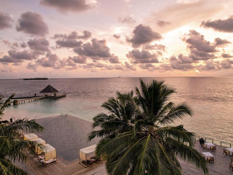 Pool und Palmen mit Blick auf das Meer bei Sonnenuntergang in einem tropischen Resort.