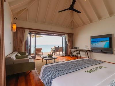 Hotelzimmer mit Meerblick, komfortablem Bett, Sofa, Schreibtisch und Outdoor-Bereich am Wasser.