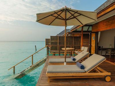 Holzsteg mit Liegestühlen und Sonnenschirm über klarem türkisem Wasser bei bewölktem Himmel.