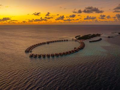 Luxuriöse Überwasserbungalows im Herzen eines tropischen Atolls bei Sonnenuntergang.