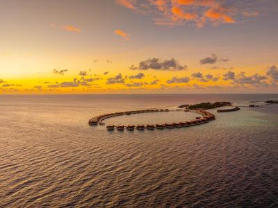 Bungalows auf Stelzen im Meer bei Sonnenuntergang mit buntem Himmel.
