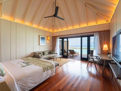 Helles Hotelzimmer mit Holzfußboden, großem Bett und Blick auf das Meer durch bodentiefe Fenster.