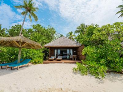 Bungalow am Strand mit Sand, Liegen und Palmen umgeben von grünem Laub.