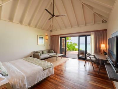 Geräumiges Hotelzimmer mit Doppelbett, Sofa, Schreibtisch und Blick auf eine Terrasse mit Meerblick.