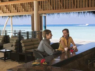 Zwei Personen sitzen an einer Bar mit Blick auf das Meer unter einem Dach aus Stroh.