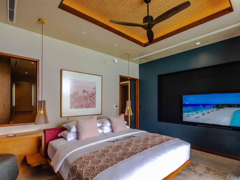 Modernes Schlafzimmer mit großem Bett, Deckenventilator und eingebautem Fernseher an der Wand.