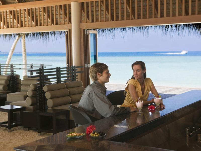 Zwei Personen sitzen an einer Bar mit Blick auf das Meer unter einem Dach aus Stroh.