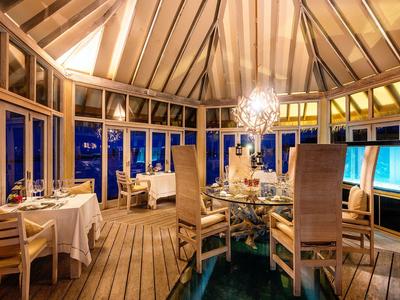 Elegantes Restaurant mit Holzdecke und großen Fenstern, stimmungsvoll beleuchtet am Abend.