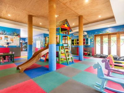 Bunter Indoor-Spielbereich mit Rutsche, Klettergerüst und Stühlen bei Tageslicht.