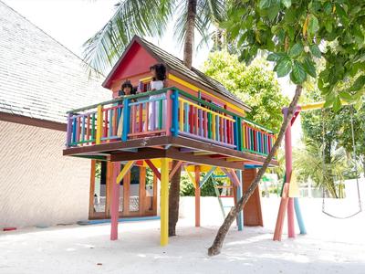 Buntes Baumhaus auf Stelzen unter Bäumen in einem sonnigen Urlaubsort.
