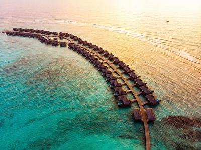 Reihen von über Wasser gebauten Bungalows in einem tropischen Resort umgeben von klarem, türkisfarbenem Wasser.