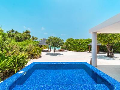 Blauer Pool vor einer Terrasse mit weißen Säulen und grünem Garten unter blauem Himmel.