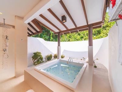 Freiluft-Whirlpool auf einer Terrasse mit weißen Wänden und Holzbalkendecke.