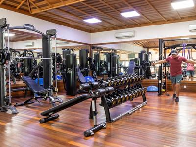 Moderne Fitnessstudio mit Hanteln, Trainingsgeräten und Spiegelwand auf Holzboden.