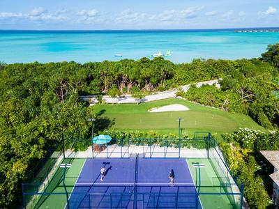 Blick auf Tennisplatz neben Golfplatz und tropischem Meer im Hintergrund.