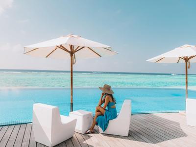Frau in blauem Kleid sitzt unter Sonnenschirm am Pool mit Meerblick.