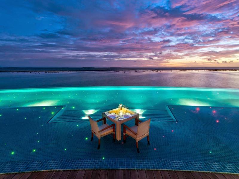 Tisch mit zwei Stühlen im Infinity-Pool bei Sonnenuntergang am Meer.