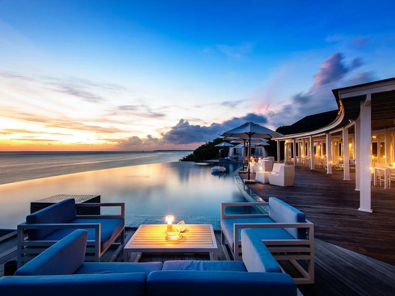 Luxuriöse Terrasse mit Sofa und Tisch neben Infinity-Pool bei Sonnenuntergang am Strand