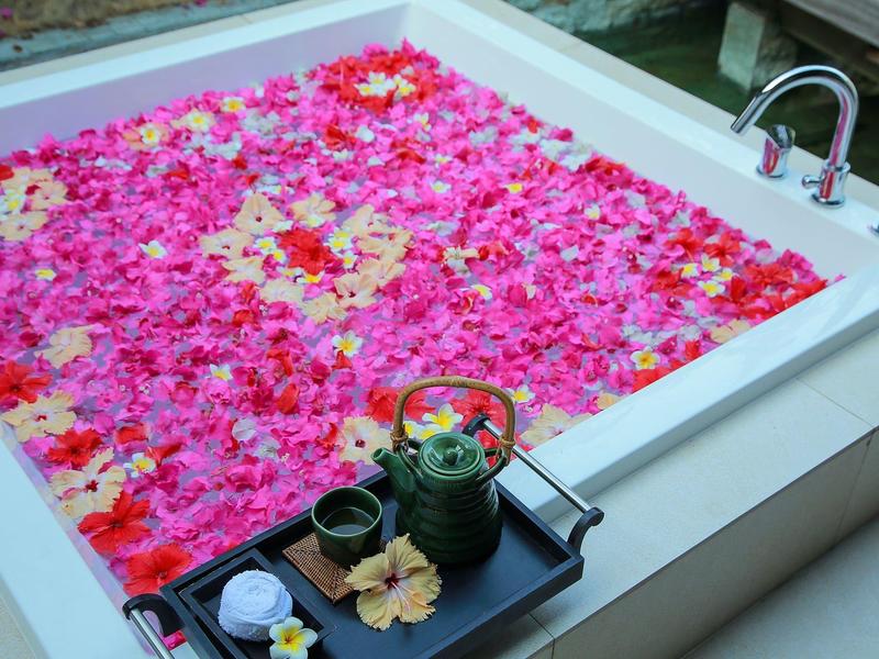 Whirlpool mit bunten Blütenblättern und Tee-Set am Rand in einem entspannten Ambiente.