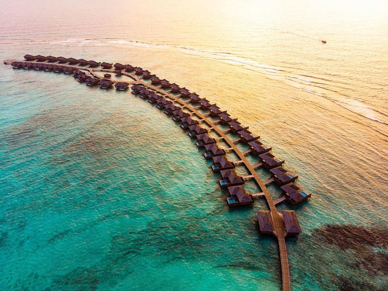 Reihen von über Wasser gebauten Bungalows in einem tropischen Resort umgeben von klarem, türkisfarbenem Wasser.