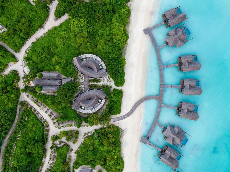 Luftaufnahme eines Resorts mit Bungalows über Wasser und tropischem Grünland am Strand.