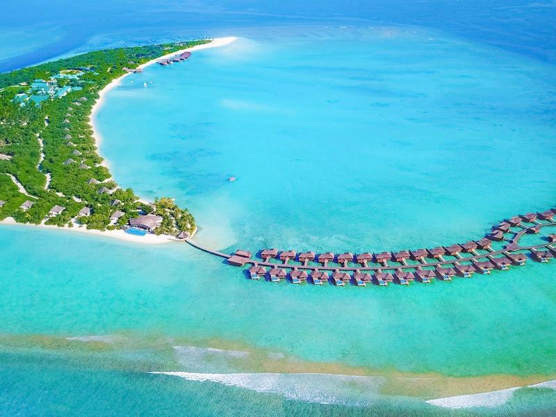 Luftaufnahme einer tropischen Insel mit über Wasser gebauten Bungalows in klarem blauem Wasser