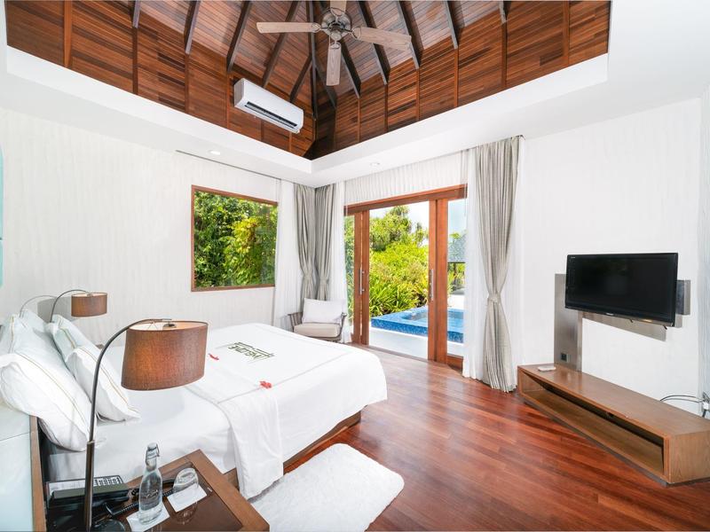 Helles Hotelzimmer mit Holzboden, Doppelbett, TV und Blick auf Pool durch große Fenster.