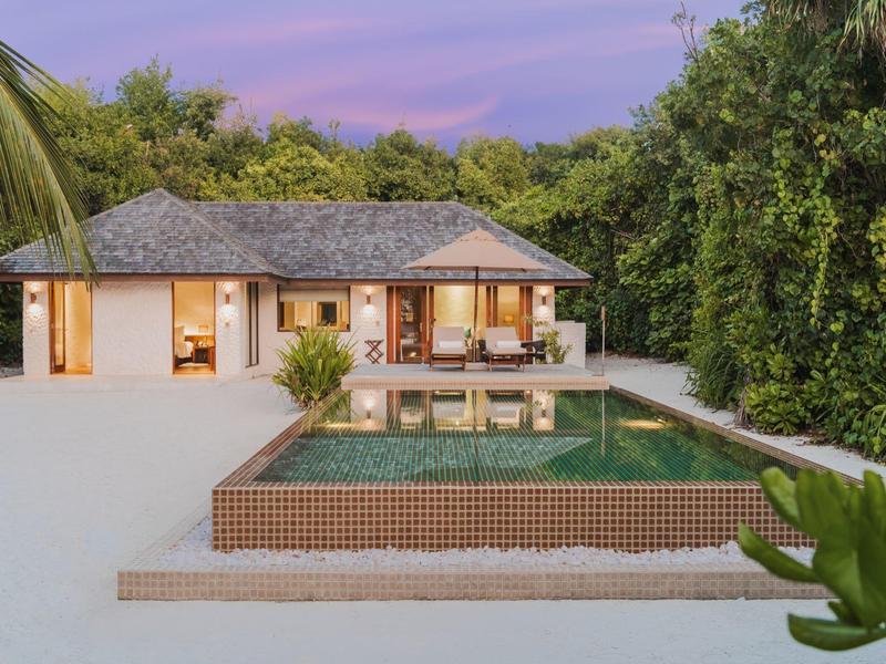 Luxuriöse Villa mit Pool und umgeben von üppigem Grün bei Sonnenuntergang.