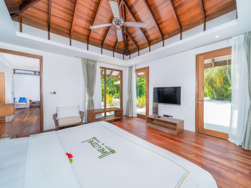 Modernes Hotelzimmer mit Holzboden, Deckenventilator und großem Fenster mit Blick auf tropische Pflanzen.