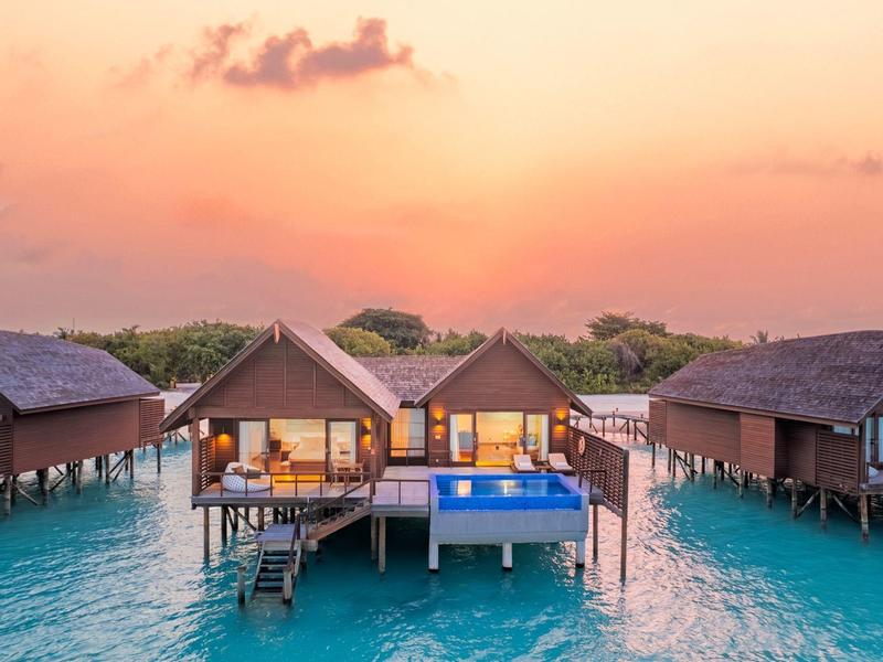 Überwasserbungalows auf Pfählen mit Sonnenuntergang am klaren türkisfarbenen Wasser