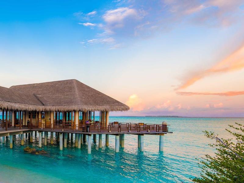 Über dem ruhigen Meer errichtete Bungalows bei Sonnenuntergang mit klarem Himmel.