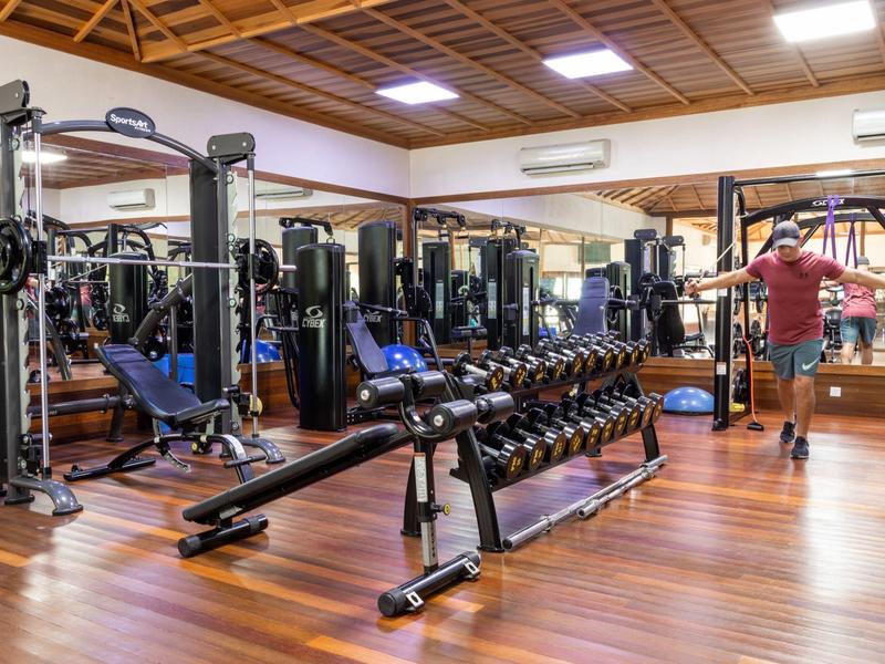 Modern ausgestatteter Fitnessraum mit Gewichten, Hanteln und Spiegeln auf Holzboden.