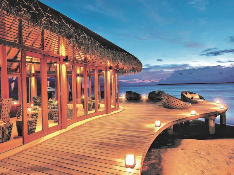 Strandhotel mit Holzsteg und gemütlicher Beleuchtung bei Sonnenuntergang