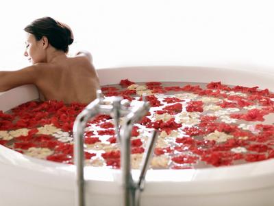 Frau entspannt in weißer Badewanne mit Wasser und roten sowie weißen Rosenblättern.