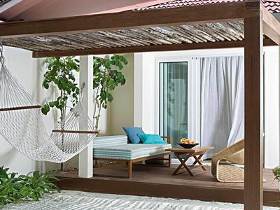 Gemütliche Terrasse mit Holzboden, weißem Hängesessel, Sitzbank und Kissen neben Glas-Schiebtür.