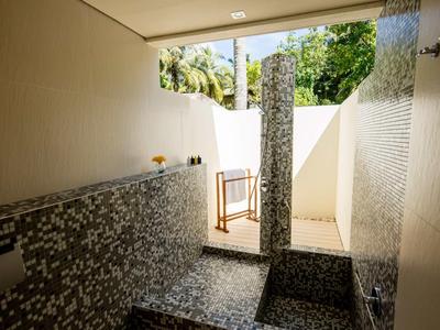 Moderner Wellnessbereich mit Mosaikfliesen, Dusche und natürlichem Tageslicht durch offene Wand.