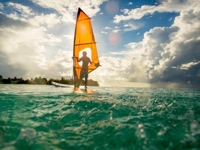 Persoon die windsurft op turquoise water onder een bewolkte lucht.