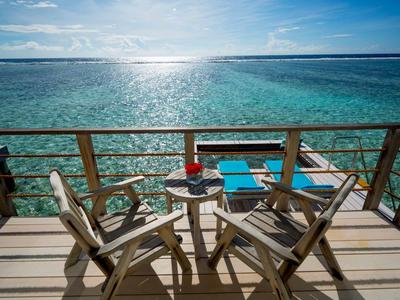 Holzterrasse mit zwei Stühlen, kleinem Tisch und Blick auf türkisblaues Meer bei sonnigem Himmel.