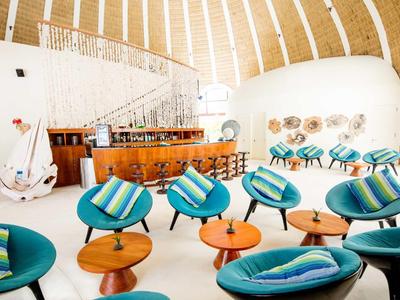 Moderne Lounge mit blauen Sesseln, Holztischen, Bar und geschwungener Treppe in heller, luftiger Halle.