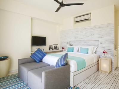 Helles Schlafzimmer mit großem Bett, grauem Sofa, Wand-TV und Deckenventilator in modernem Stil.