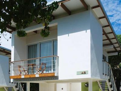 Modernes, weißes Hochhaus mit offenem Untergeschoss, Holzgeländer und grünen Pflanzen unter blauem Himmel.