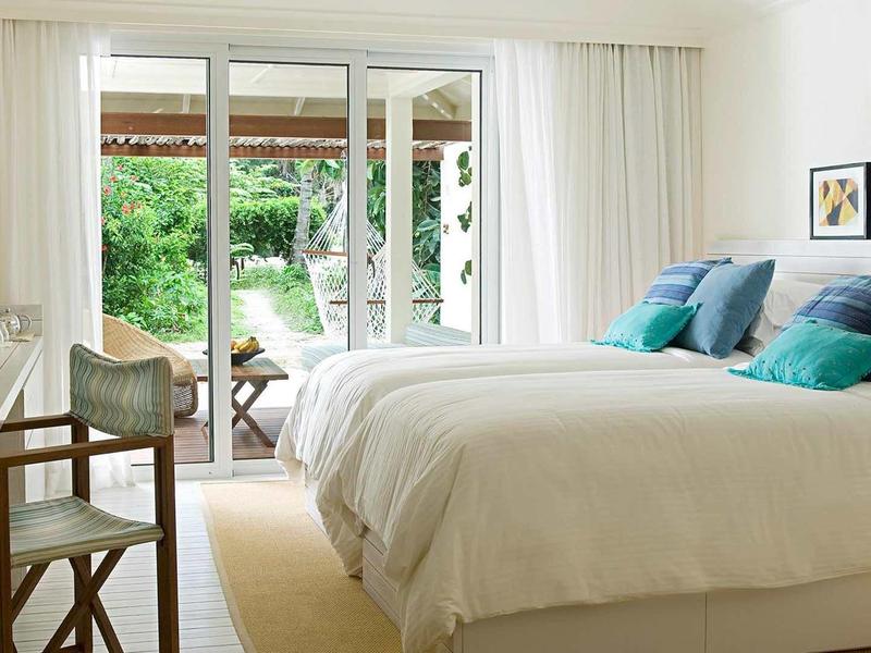 Helles Schlafzimmer mit Doppelbett, weißen Vorhängen, Holzmöbeln und Blick in den Garten.