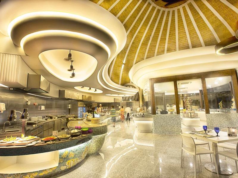 Modernes Café mit geschwungenen Decken, heller Einrichtung und Glastischen, Licht wirkt warm.